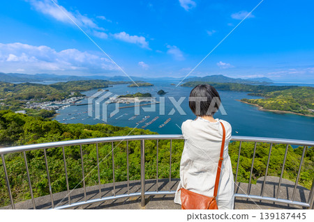 A woman's back as she gazes at the scenery from Hario Park on Nagashima Island in Kagoshima Prefecture; a moment of solace for a woman traveling amidst breathtaking views. A woman's back as she gazes at the scenery from Hario Park on Nagashima Island in Kagoshima Prefecture; a moment of solace for a woman traveling amidst breathtaking views. 139187445