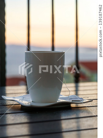 Quiet drink moment with sea view at sunset. White cup with tea tag a balcony table. Adriatic sea in Makarska, Croatia in blurred background. Quiet drink moment with sea view at sunset. White cup with tea tag a balcony table. Adriatic sea in Makarska, Croatia in blurred background. 139187462