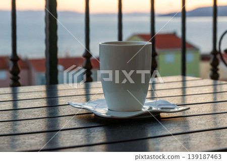 Quiet drink moment with sea view at sunset. White cup with tea tag a balcony table. Adriatic sea in Makarska, Croatia in blurred background. 139187463