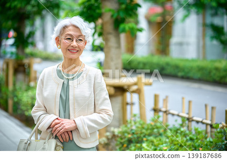 一位優雅的老婦人在城市綠植的襯托下面帶微笑。 一位優雅的老婦人在城市綠植的襯托下面帶微笑。 139187686