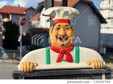 Colorful chef mascot sign standing near a residential street. Restaurant advertising, small business identity, street decor, hospitality, and local food service. Colorful chef mascot sign standing near a residential street. Restaurant advertising, small business identity, street decor, hospitality, and local food service. 139187744