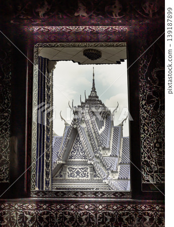 Looking through a dark, intricately patterned portal, the eye is drawn to the luminous peaks of the sanctuary, which rise like a ceramic mirage against the pale sky of Wat Paknam Kham Nu "Blue 139187899