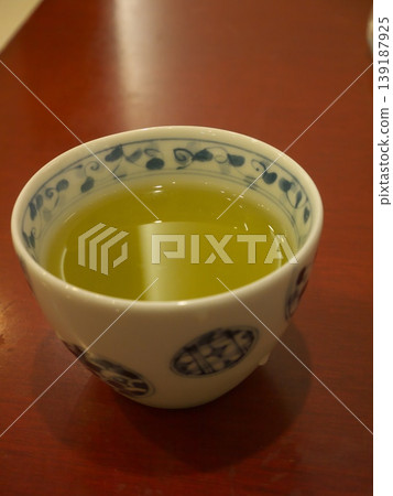 Green tea in a teacup with a arabesque pattern, placed on a wood-grain table. Green tea in a teacup with a arabesque pattern, placed on a wood-grain table. 139187925