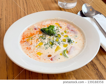 Close up creamy vegetable soup with broccoli florets, herbs and oil drops in white plate. Healthy nutrition, comfort meal, food texture and homemade cooking concept. Close up creamy vegetable soup with broccoli florets, herbs and oil drops in white plate. Healthy nutrition, comfort meal, food texture and homemade cooking concept. 139188358