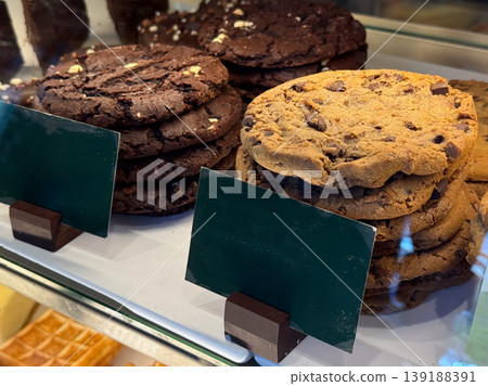 Chocolate cookies stack and bakery biscuits in showcase. Sweet snack, dessert selection, sugar intake, baked goods display, and confectionery assortment in cafe environment. Chocolate cookies stack and bakery biscuits in showcase. Sweet snack, dessert selection, sugar intake, baked goods display, and confectionery assortment in cafe environment. 139188391