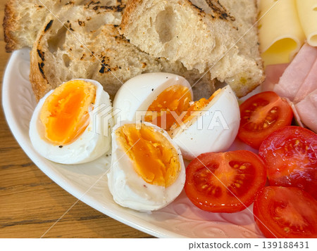 Close view of boiled eggs with tomato, grilled bread, ham and cheese on a white plate. Breakfast detail, yolk texture, protein food, cafe dining, morning nutrition and fresh ingredient variety. Close view of boiled eggs with tomato, grilled bread, ham and cheese on a white plate. Breakfast detail, yolk texture, protein food, cafe dining, morning nutrition and fresh ingredient variety. 139188431