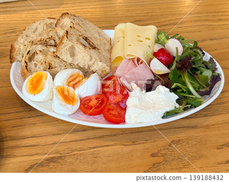 Close-up assorted breakfast plate with eggs, tomato, cheese, ham, salad, radish, cream and grilled bread on a wooden table. Balanced brunch, cafe meal, protein, dairy, vegetable and bakery serving. Close-up assorted breakfast plate with eggs, tomato, cheese, ham, salad, radish, cream and grilled bread on a wooden table. Balanced brunch, cafe meal, protein, dairy, vegetable and bakery serving. 139188432