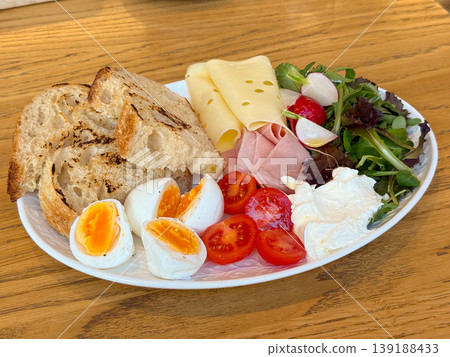 Assorted breakfast plate with eggs, tomato, cheese, ham, salad, radish, cream and grilled bread on a wooden table. Balanced brunch, cafe meal, protein, dairy, vegetable and bakery serving. Assorted breakfast plate with eggs, tomato, cheese, ham, salad, radish, cream and grilled bread on a wooden table. Balanced brunch, cafe meal, protein, dairy, vegetable and bakery serving. 139188433