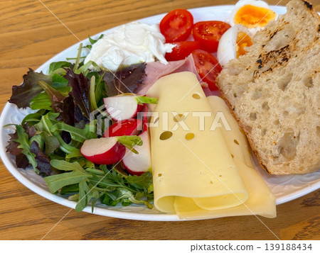 Breakfast plate with emmental cheese, ham, egg, tomato, radish, salad, cream and grilled bread on a wooden table. Morning meal, cafe dining, protein, vegetable variety and brunch nutrition. 139188434