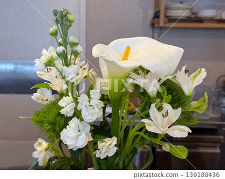 White calla lily bouquet with alstroemeria, stock flower and green dianthus on a cafe counter. Floral freshness, table decoration, botanical texture, elegant interior detail and calm natural styling. White calla lily bouquet with alstroemeria, stock flower and green dianthus on a cafe counter. Floral freshness, table decoration, botanical texture, elegant interior detail and calm natural styling. 139188436