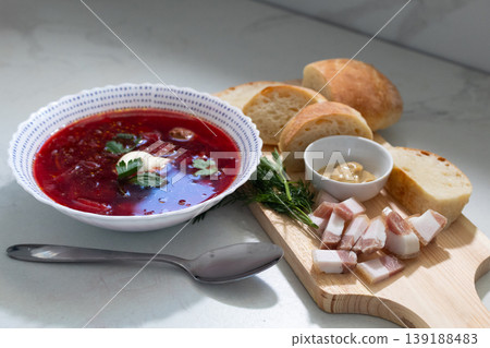 Bowl of traditional borscht soup topped with sour cream and fresh dill garnish. Served with rustic bread slices and smoked bacon on wooden Bowl of traditional borscht soup topped with sour cream and fresh dill garnish. Served with rustic bread slices and smoked bacon on wooden 139188483