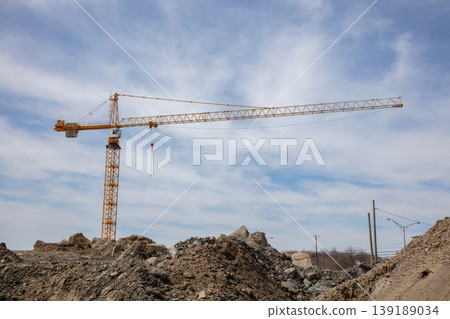 Tower crane at construction site with dirt mounds and cloudy blue sky Tower crane at construction site with dirt mounds and cloudy blue sky 139189034