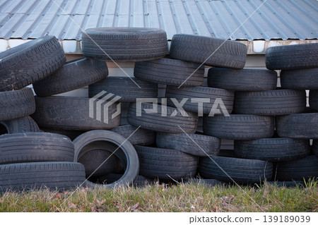Pile of used car tires stacked outdoors against metal wall, recycling concept 139189039