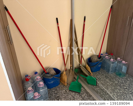 Cleaning tools and water containers stored in a small interior space. Household maintenance, sanitation routine, storage organization, and domestic utility area. 139189094