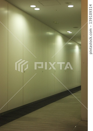 A view of the long corridor and wall panels of a modern facility illuminated by downlights. 139189314