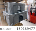 Two grey fabric storage bins with clear windows and zippers are stacked on a shelf in a store. They feature a herringbone pattern, offering an organized and stylish solution for home wardrobe storage 139189477