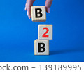 B2B, business to business marketing symbol. Concept word B2B on wooden blocks. Beautiful blue background. Businessman hand. Business and B2B concept. Copy space 139189995