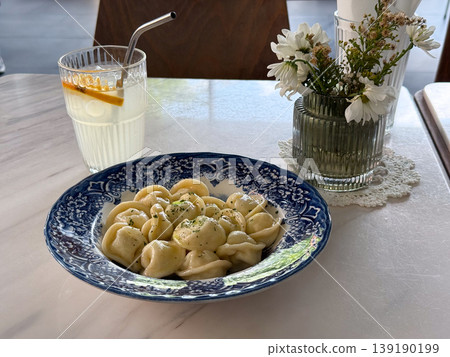 Plate of dumplings with drink and flower vase on marble table in cafe interior setting. Dining experience, food styling, hospitality service, casual meal and aesthetic composition. Plate of dumplings with drink and flower vase on marble table in cafe interior setting. Dining experience, food styling, hospitality service, casual meal and aesthetic composition. 139190199