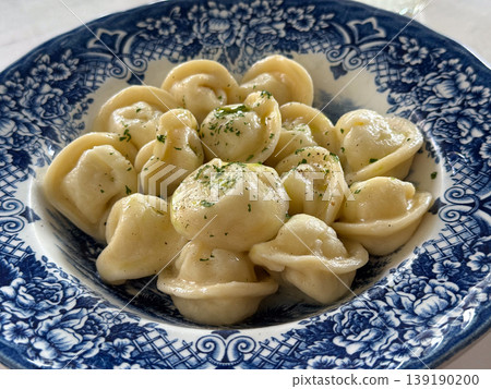 Plate of dumplings with butter and herbs served on blue patterned dish in restaurant setting. Russian cuisine, food presentation, lunch meal, comfort eating and gastronomy culture. Plate of dumplings with butter and herbs served on blue patterned dish in restaurant setting. Russian cuisine, food presentation, lunch meal, comfort eating and gastronomy culture. 139190200