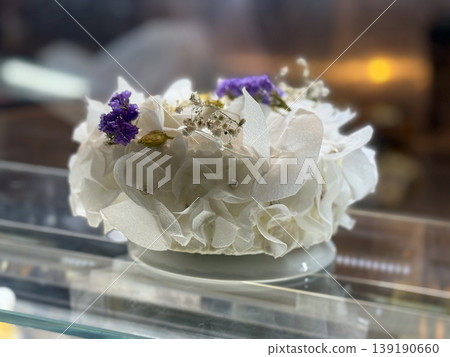 White floral decorated cake with edible flowers in bakery showcase. Celebration dessert, botanical decoration, confectionery art, elegant pastry design, and festive presentation concept. White floral decorated cake with edible flowers in bakery showcase. Celebration dessert, botanical decoration, confectionery art, elegant pastry design, and festive presentation concept. 139190660