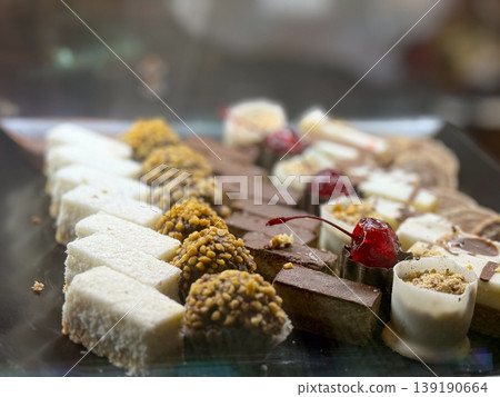 Assorted small pastries and sweets arranged on tray in bakery showcase. Dessert variety, confectionery selection, texture diversity, sweet assortment, and retail food display concept. Assorted small pastries and sweets arranged on tray in bakery showcase. Dessert variety, confectionery selection, texture diversity, sweet assortment, and retail food display concept. 139190664