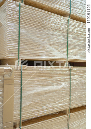Close-up of stacked wooden planks secured with straps. Construction timber stored for transport or sale, showing natural texture and grain of processed wood material. Close-up of stacked wooden planks secured with straps. Construction timber stored for transport or sale, showing natural texture and grain of processed wood material. 139191103