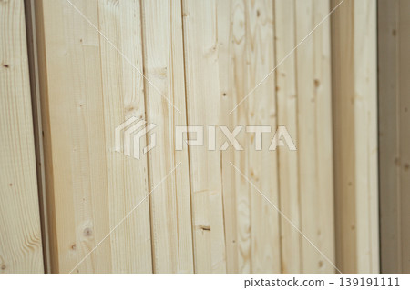 Close-up of vertical wooden wall panels with natural grain. Decorative cladding used in interiors, showcasing clean lines and warm organic texture. Close-up of vertical wooden wall panels with natural grain. Decorative cladding used in interiors, showcasing clean lines and warm organic texture. 139191111