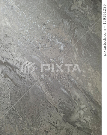 A brushed silver metallic surface displays a wavy texture with reflections. Light hits the surface, creating shiny patterns and variations in depth and tone. A brushed silver metallic surface displays a wavy texture with reflections. Light hits the surface, creating shiny patterns and variations in depth and tone. 139191259