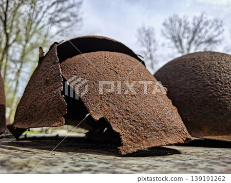 Close up view of old military helmets with rust and signs of wear. These helmets lie on a rough surface, highlighting their history and showing the effects of time and weather. Close up view of old military helmets with rust and signs of wear. These helmets lie on a rough surface, highlighting their history and showing the effects of time and weather. 139191262