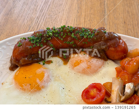Sausage with sauce and fried eggs topped with chive on a breakfast plate. Protein meal, cooking method, morning nutrition, savory flavor, and restaurant serving style. Sausage with sauce and fried eggs topped with chive on a breakfast plate. Protein meal, cooking method, morning nutrition, savory flavor, and restaurant serving style. 139191265