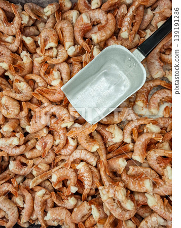 A top view shows a large pile of frozen pink shrimps in a grocery store. A metal scoop sits among the shrimps, indicating they are for sale by weight. A top view shows a large pile of frozen pink shrimps in a grocery store. A metal scoop sits among the shrimps, indicating they are for sale by weight. 139191286