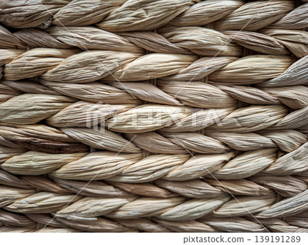 This close up shows a woven texture of natural light brown wicker made of dried plant fibers. The image displays the organic braided pattern and details of the material. 139191289