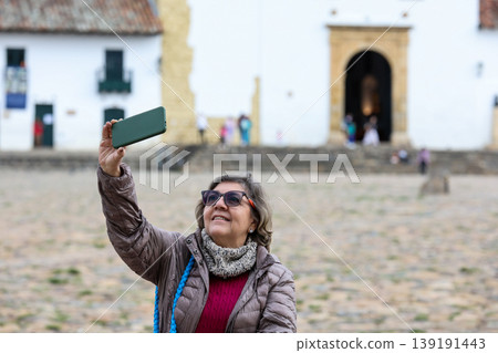 Happy senior woman concept. Senior travel concept. Senior woman taking selfies at the beautiful colonial town of Villa de Leyva in Colombia Happy senior woman concept. Senior travel concept. Senior woman taking selfies at the beautiful colonial town of Villa de Leyva in Colombia 139191443