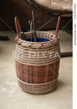 Two tone wicker storage basket holding garden tools on patio Two tone wicker storage basket holding garden tools on patio 139191468