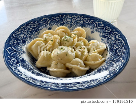 Plate of dumplings with butter and herbs served on blue patterned dish in restaurant setting. Russian cuisine, food presentation, lunch meal, comfort eating and gastronomy culture. Plate of dumplings with butter and herbs served on blue patterned dish in restaurant setting. Russian cuisine, food presentation, lunch meal, comfort eating and gastronomy culture. 139191510