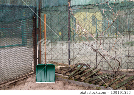 green plastic snow shovel leaning against a wire mesh fence in the garden area during spring green plastic snow shovel leaning against a wire mesh fence in the garden area during spring 139191533