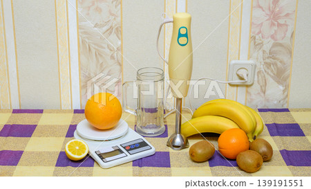 preparing a fruit smoothie using a hand blender and scales on a checkered tablecloth 139191551