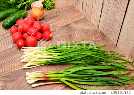 bunches of green onions and garlic next to a pile of radishes on a brown wooden surface bunches of green onions and garlic next to a pile of radishes on a brown wooden surface 139191572