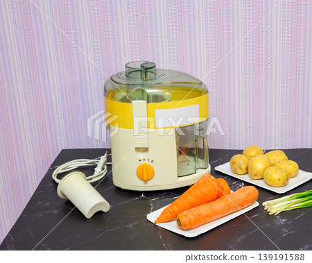 beige juicer on the table next to washed potatoes, carrots and green onions 139191588