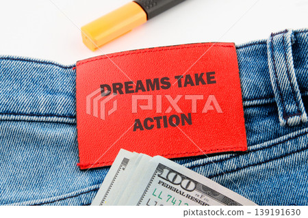 Red Dreams Take Action label on blue jeans with US hundred dollar bills and a yellow marker, all on a clean white background 139191630
