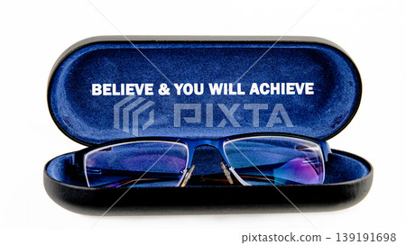 A pair of blue framed eyeglasses lies open in a dark blue velvet case. The case lid shows the words BELIEVE YOU WILL ACHIEVE A pair of blue framed eyeglasses lies open in a dark blue velvet case. The case lid shows the words BELIEVE YOU WILL ACHIEVE 139191698