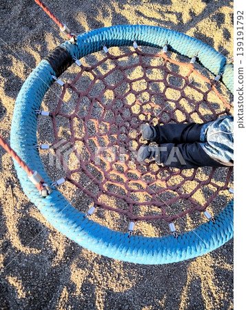 A child swings on a round wicker swing called Nest at a playground A child swings on a round wicker swing called Nest at a playground 139191792