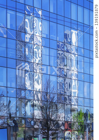 Glass facade with blue window grid with reflection of towers, tree silhouettes, urban architecture. Abstract blurred urban reflection, business, city design, corporate exterior, real estate background Glass facade with blue window grid with reflection of towers, tree silhouettes, urban architecture. Abstract blurred urban reflection, business, city design, corporate exterior, real estate background 139191879
