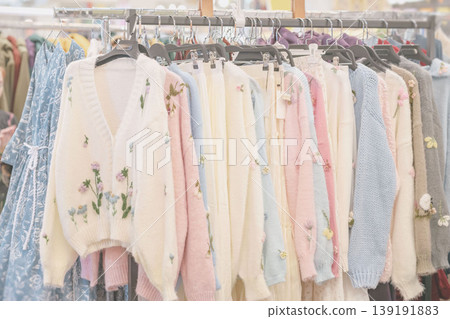 Clothing rack displays knit cardigans, sweaters, dresses, hangers, and floral embroidery in retail store. Concept of handmade clothing, boutique fashion, shopping, wardrobe, textile, apparel sales Clothing rack displays knit cardigans, sweaters, dresses, hangers, and floral embroidery in retail store. Concept of handmade clothing, boutique fashion, shopping, wardrobe, textile, apparel sales 139191883