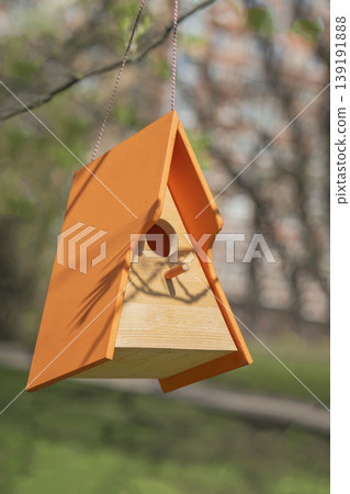 Wooden birdhouse with orange roof hangs from tree branch in garden, showing birdhouse entrance hole and perch. Concept of birdhouse, spring, wildlife shelter, garden decor, nesting support Wooden birdhouse with orange roof hangs from tree branch in garden, showing birdhouse entrance hole and perch. Concept of birdhouse, spring, wildlife shelter, garden decor, nesting support 139191888