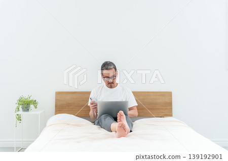 Middle-aged men using smartphones and computers in bed. Middle-aged men using smartphones and computers in bed. 139192901