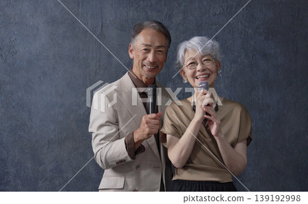 Senior men and women singing karaoke, black background, portrait, looking at camera Senior men and women singing karaoke, black background, portrait, looking at camera 139192998