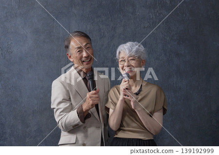 Senior men and women singing karaoke, black background, portrait, looking at camera Senior men and women singing karaoke, black background, portrait, looking at camera 139192999