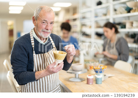 Mature potter demonstrates a clay cup he made with his own hands 139194239