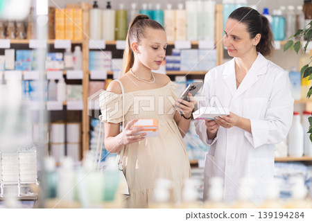 Pregnant girl in summer clothes scans code on package of pills to check expiration date. Female pharmacist helps to choose right pills Pregnant girl in summer clothes scans code on package of pills to check expiration date. Female pharmacist helps to choose right pills 139194284